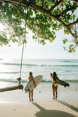Tailslide_two girl surfers walking with boards on Madiha beach_learn to surf any wave anywhere_Retreat