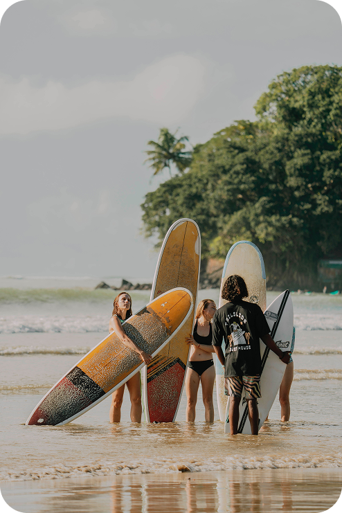 Tailslide surf retreat_girl learning how to surf surfer walking with board through greenery towards Madiha beach_quiet surf town Sri Lanka location_Home